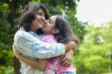 Young indian mother hugging her daughter kissing at summer park spending time together. bonding , playful, Fun childhood, mothers day