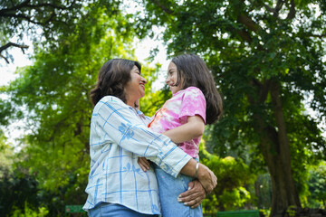 Fototapeta premium Young indian mother carrying, holding her daughter on shoulder spending time together. bonding , playful interaction , holiday, vacation concept.