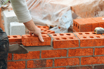 Bricklayer crafting a sturdy wall with red bricks at a construction site on a sunny afternoon