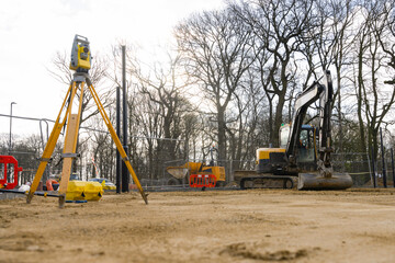 Construction site with heavy machinery and surveying equipment under a cloudy sky in early spring