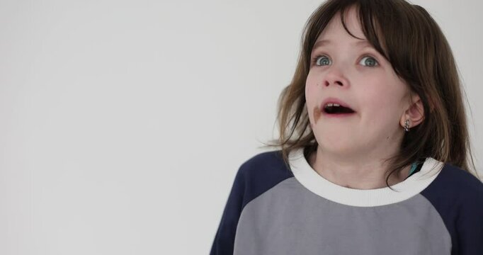 Young schoolgirl with birthmark expresses astonishment looking from side to side against white. Emotional little girl with surprised facial expression