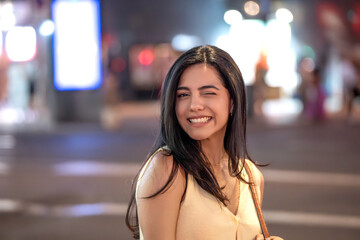 Young woman is winking and smiling while standing outdoors on a city street at night