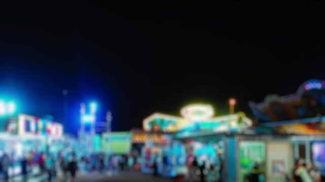Dreamy nighttime at an amusement park, blurred neon lights creating magical vibe. Silhouetted visitors explore the vibrant midway, rides and attractions paint the darkness in color. Panning shot.
