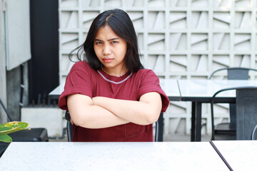 irritated asian woman sitting in cafe with crossed hand looking at camera