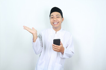 pleased asian muslim man smiling while presenting hand to beside with holding mobile phone isolated