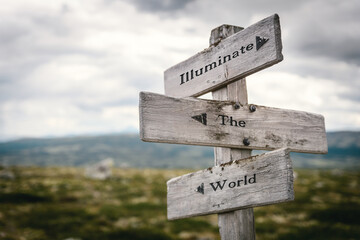 illuminate the world text quote written on wooden signpost at the crossroads outdoors in nature.