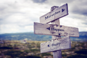 miracles happen daily text quote written on wooden signpost at the crossroads outdoors in nature.