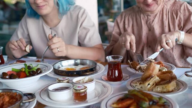 two women are laughing and talking as they eat, clearly enjoying each other's company. Turkish Breakfast, Sunday breakfast or brunch with feta cheese and eggs, Turkish meal served in restaurant