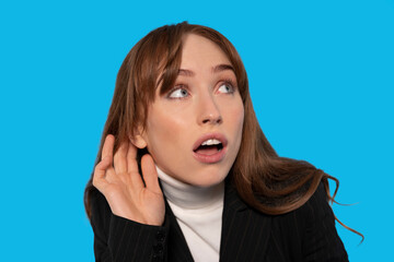 Curious woman listens intently on a vibrant blue background while wearing a stylish outfit in a...