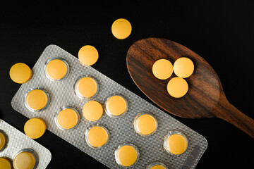 Pills Medicine tablet capsules blister pack in wooden spoon on a black background
