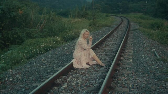 A woman sits along the railway tracks in a beautiful and peaceful landscape, enjoying the splendour of nature
