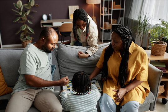 African American family engaging in board game activity with children in cozy living room setting, surrounded by modern decor and warm ambiance - Powered by Adobe