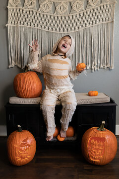 Child in mummy costume posing with pumpkins in Halloween scene indoors