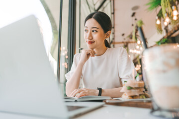 Fototapeta premium Adult business asian woman thinking for idea writing daily journal at indoors cafe