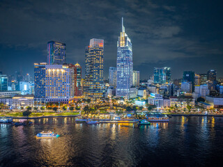 Aerial night view of Ho Chi Minh City, Vietnam. Skyscrapers and other high-rise buildings at downtown. Colorful city lights reflected in water of the Saigon River.