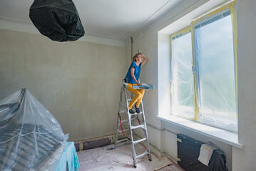 Exhausted woman resting on stepladder after plastering walls in new flat. Tired girl sitting in a...