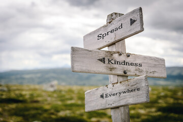 spread kindness everywhere text quote written on wooden signpost at the crossroads outdoors in nature.