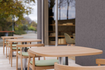 A minimalist contemporary cafe features an outdoor patio area with a row of wooden tables.