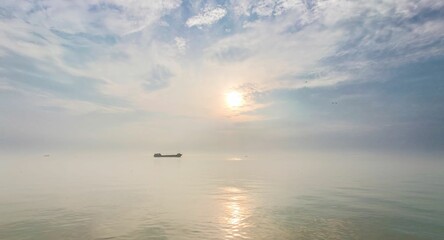 Serene sunrise over calm sea with distant ship.