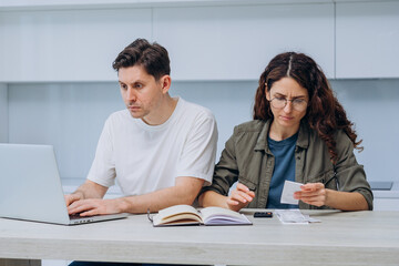 Obraz premium Young couple is sitting at their kitchen table, managing their finances together and looking concerned as they review bills and bank statements