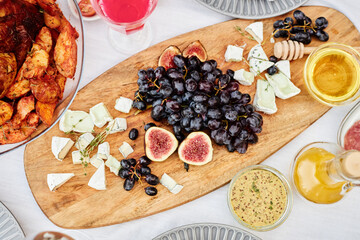 Top view background image of wooden charcuterie board with cheeses and gourmet snacks figs and honey on festive dinner table copy space