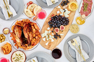 Top view background image of festive dinner table with delicious roasted chicken dish and charcuterie board on crisp white cloth shot with flash