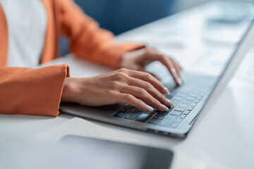 Focused businesswoman typing on a laptop in a modern office, showcasing her skills in finance, marketing, and management, highlighting teamwork and collaboration for success