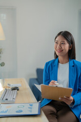 Young businesswoman is smiling while taking notes in her office. She is working on a project and seems to be having a productive day