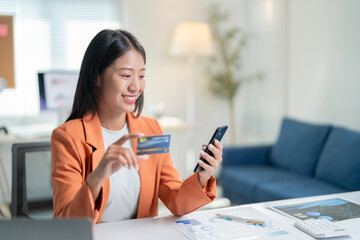 Businesswoman is smiling while using her smartphone and holding a credit card, she is making an online payment or purchasing something on the internet