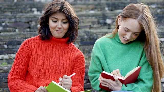 Two friends enjoying a creative afternoon in colorful sweaters, sharing ideas and writing in their journals