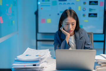 Stressed businesswoman working late in dimly lit office, typing furiously on laptop surrounded by...