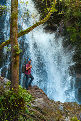 A man stands on a rock overlooking a waterfall