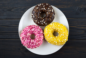 Three donuts with colored glaze and sprinkles on wooden background, top view.