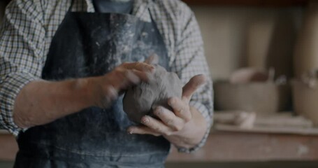 Close-up of hands of old man in apron mixing clay working in pottery studio concentrated on art. Professional occupation and creative studio concept.