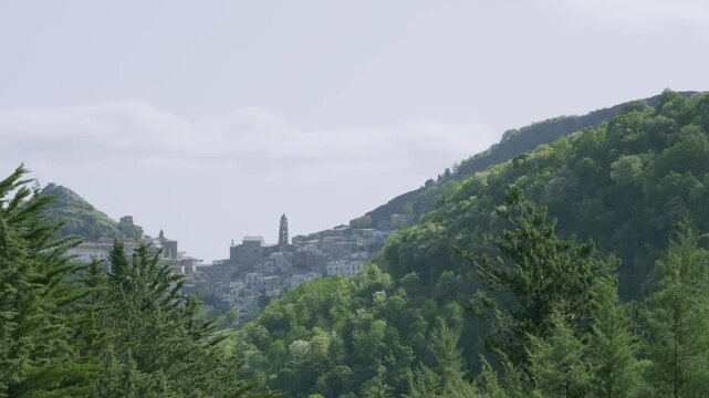 The ancient hillside town of San Fele, Italy, nestled among verdant mountains. Historic bell tower rises above buildings. Misty morning atmosphere creates dreamy, timeless scene.
