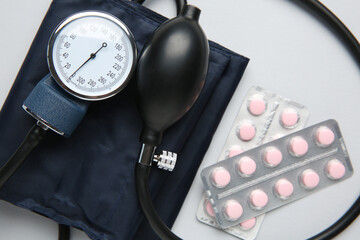 Blood pressure measuring device and pills on light grey background, top view