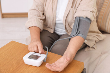 Fototapeta premium Senior woman measuring blood pressure at wooden table indoors, closeup