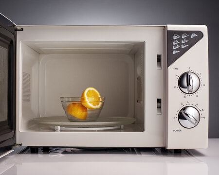Lemon in white open microwave on gray background