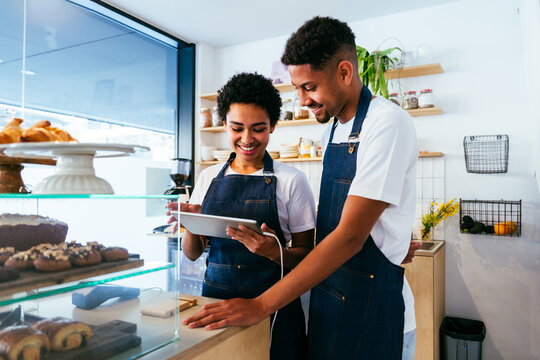 Bakery, happy portrait of hispanic black man and woman in cafe ready for serving pastry, coffee and baked foods - Confident waiter barista by counter for service, help and welcome in a coffee shop