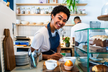 Bakery, happy portrait of black woman in cafe ready for serving pastry, coffee and baked foods. Restaurant, coffee shop and confident waiter barista by counter for service, help and welcome