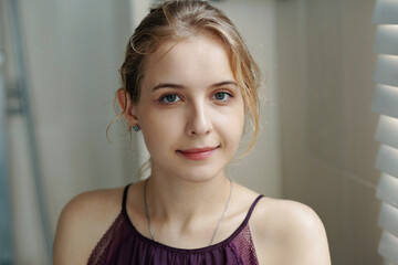 Portrait of woman looking at camera with a pleasant smile, wearing casual attire and sitting indoors surrounded by neutral colored environment