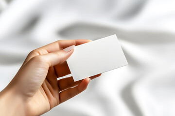 Obraz premium A hand holds a blank business card above a soft, light-colored fabric, suggesting potential for customization and branding opportunities.