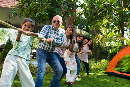Indian family of six enjoying a fun outdoor camping game of tug of war, bonding, creating memories