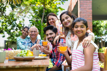 Indian family enjoying breakfast outdoors, happily posing for a group photo around the table