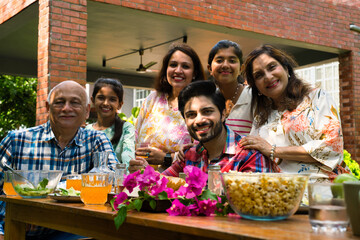 Indian family enjoying breakfast outdoors, happily posing for a group photo around the table