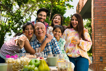 Indian family enjoying breakfast outdoors, happily posing for a group photo around the table