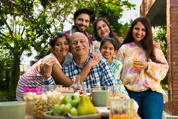Indian family enjoying breakfast outdoors, happily posing for a group photo around the table