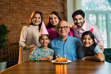 Indian family of six celebrating elderly father's birthday with cake, candle, sharing joyful moments