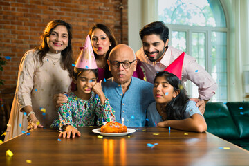 Indian family of six celebrating elderly father's birthday with cake, candle, sharing joyful moments