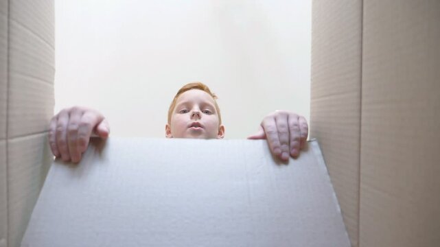 Child opening box with gift and pulling hands to take it. Little boy looks in box with emotions and feelings at face. Young kid showing joy and surprise on his face. Bottom view Slow motion